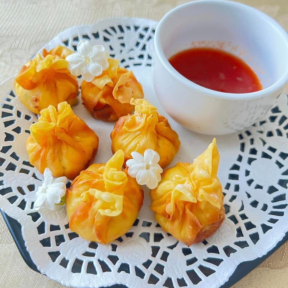 Golden fried Thai money bags with white flower garnishes and a cup of red dipping sauce.
