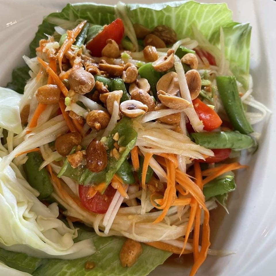 Close-up of a vibrant Thai papaya salad with peanuts, green beans, carrots, and tomatoes.