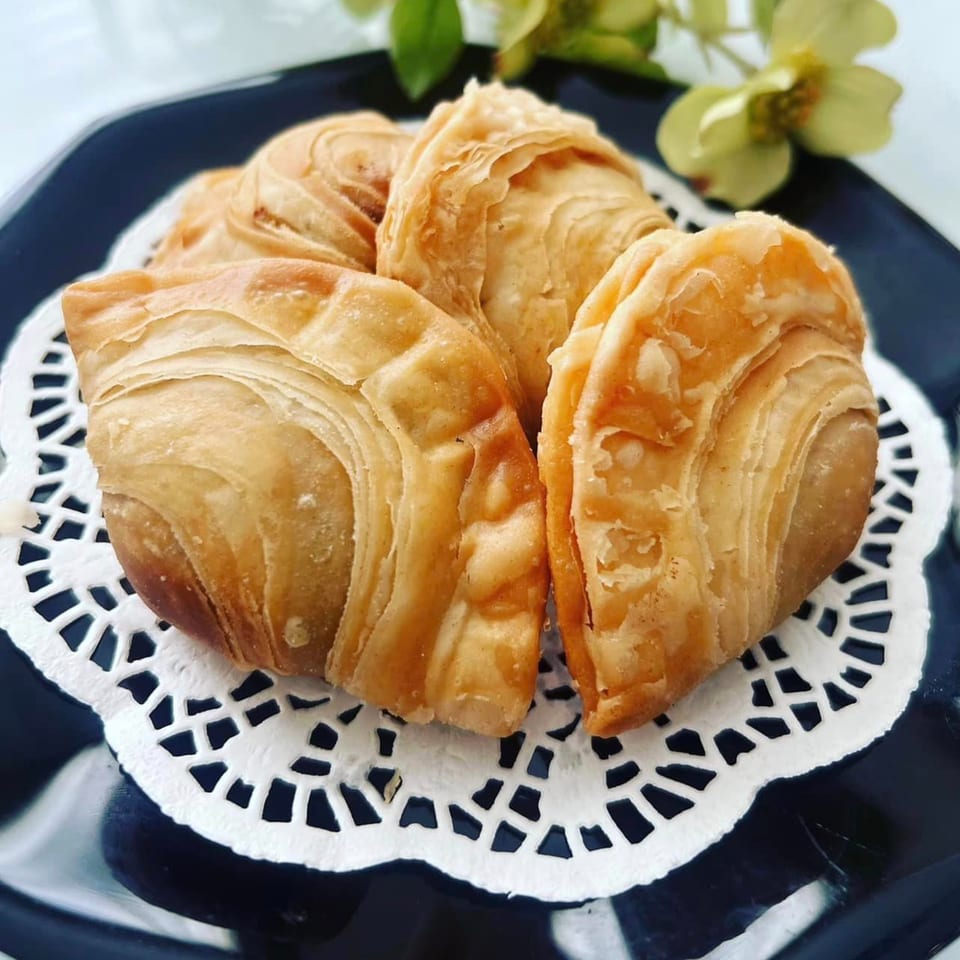 Four golden-brown Thai curry puffs with flaky pastry on a black plate with a white doily.
