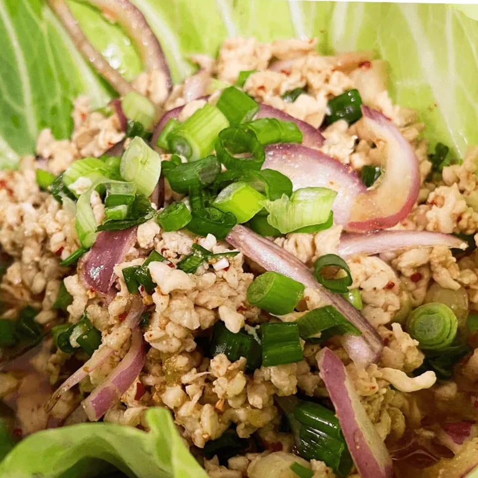 Close-up of Thai Larb Gai, a minced chicken salad with red onions and green scallions in a lettuce cup.