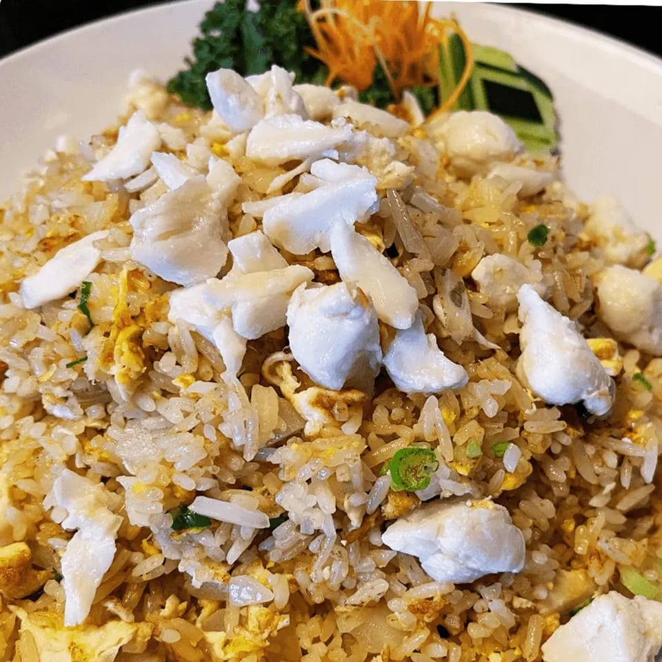 Close-up of Thai crab fried rice with egg, green onions, and shredded carrots on a white plate.