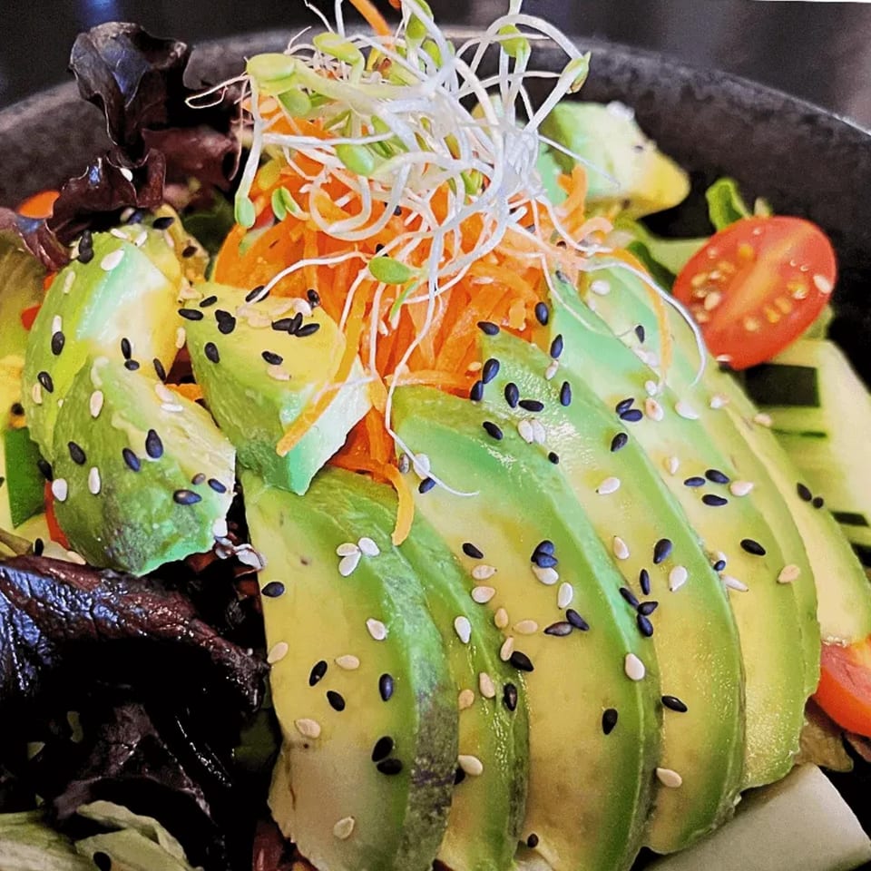A vibrant Thai salad with sliced avocado, shredded carrots, sprouts, and sesame seeds.